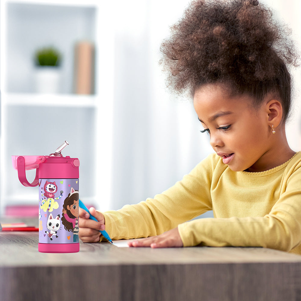 Girl sitting at a table doing homework, with a 12 ounce Gabby's Dollhouse - Pink Funtainer water bottle opened next to her.