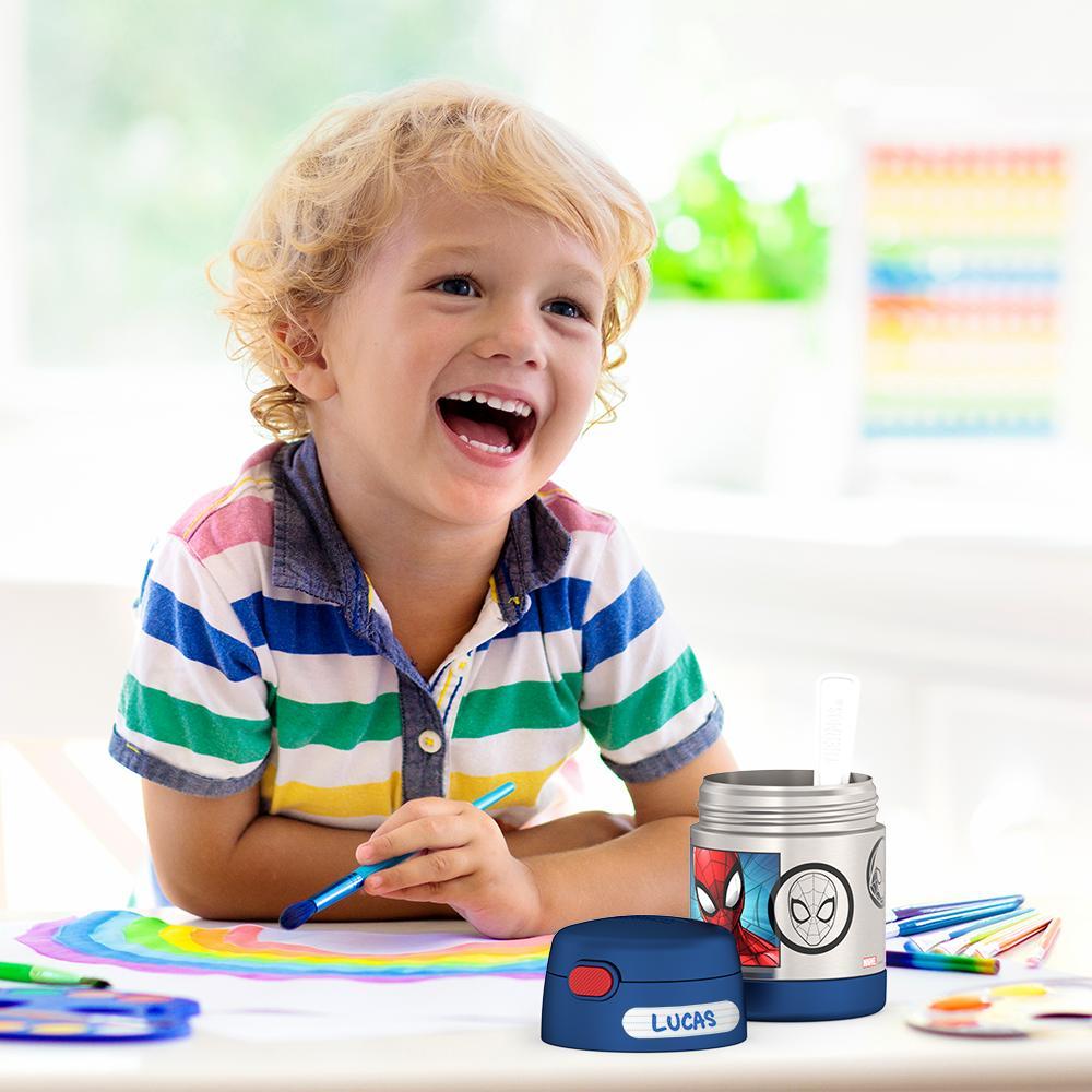 Boy smiling, sitting at table painting with an open 10 ounce Spider-Man Funtainer food jar open in front of him. 