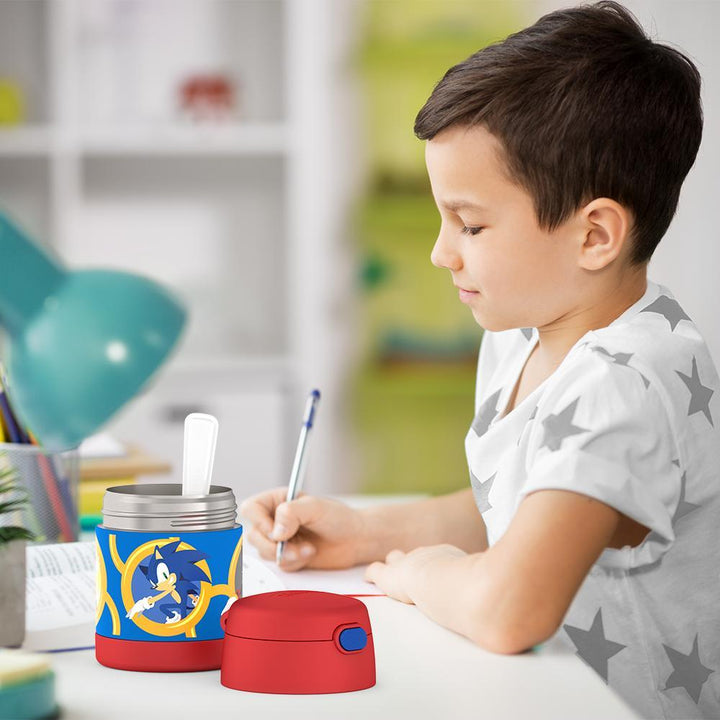 Boy sitting at table doing homework with an open 10 ounce Sonic the Hedgehog Funtainer food jar open next to him.