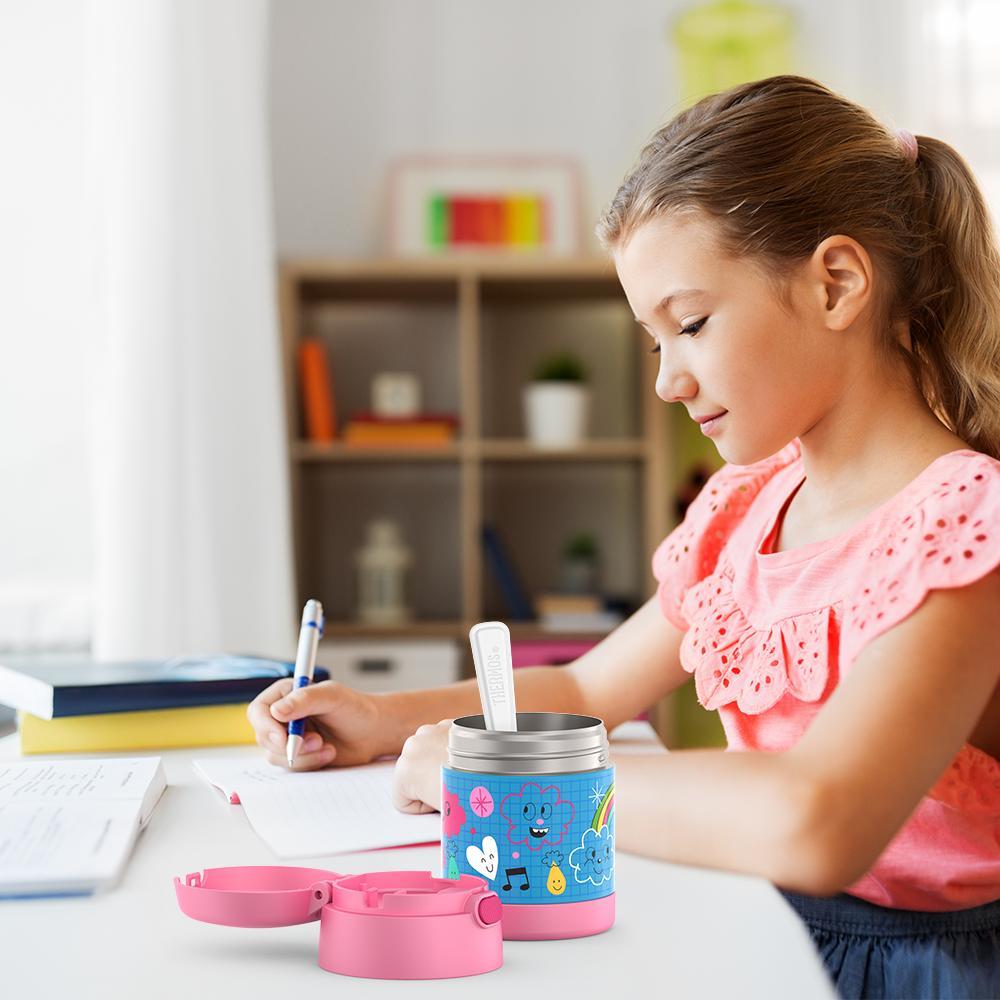 Girl sitting at table doing homework with an open 10 ounce Funtainer food jar open next to her. 