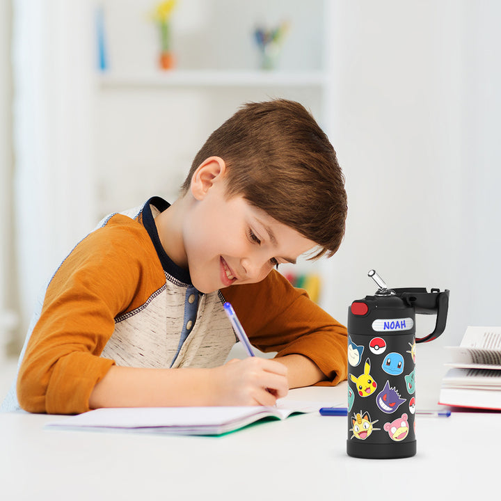 Boy sitting at a table doing homework, with the 12 ounce Funtainer Pokémon water bottle opened next to him.