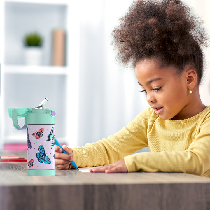 Girl sitting at a table doing homework, with a 12 ounce Butterfly Frenzy Pattern Funtainer water bottle opened next to her.