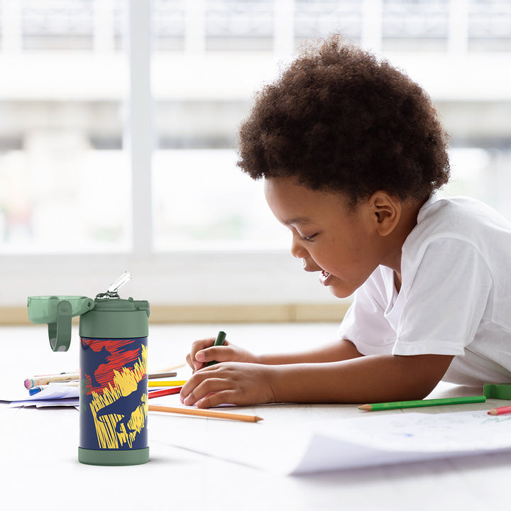 Boy sitting at a table doing homework, with the 12 ounce Funtainer dinosaur Pattern water bottle opened next to him.