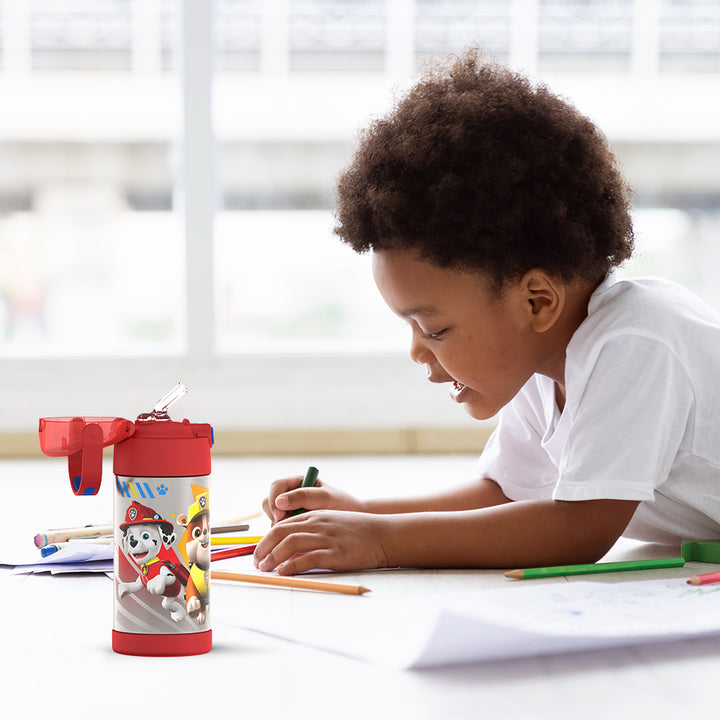 Boy sitting at a table coloring, with the 12 ounce Funtainer Paw Patrol water bottle opened next to him.