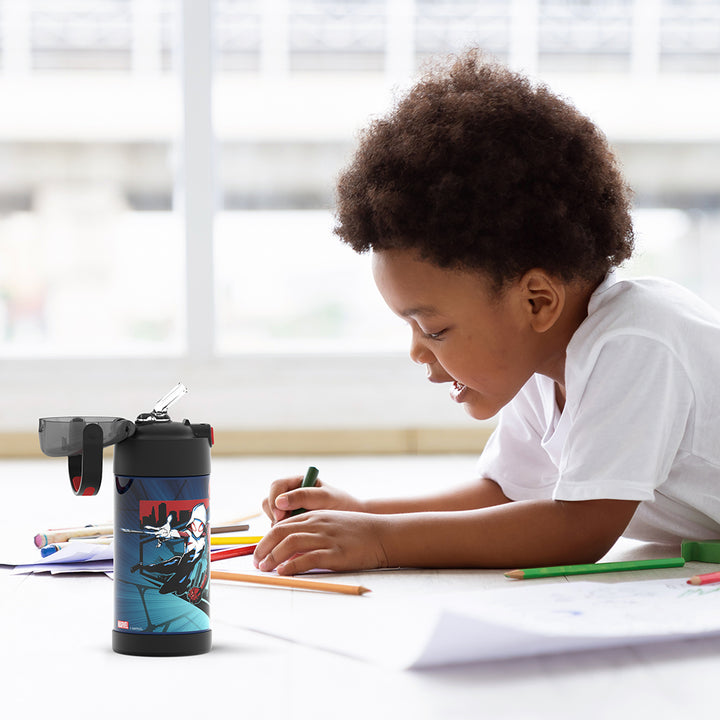 Boy sitting at a table coloring, with the 12 ounce Funtainer Spider-Man, Black and Red water bottle opened next to him.