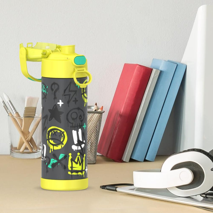 16-ounce Funtainer Stainless Steel Water Bottle with Spout and locking lid, Yellow Graffiti, side view, lid open, sitting on a table.