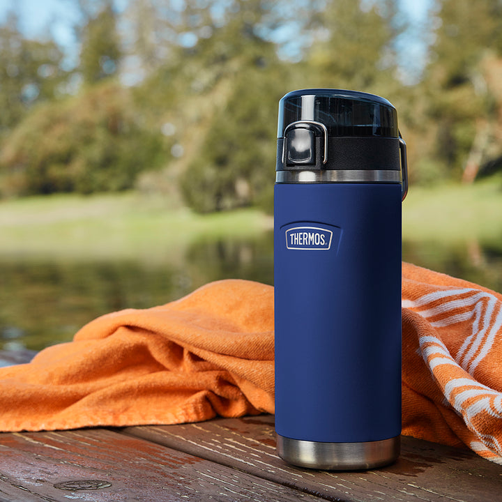 Thermos 18 ounce Stainless Steel Water Bottle with locking, covered spout lid, on a dock next to a lake.