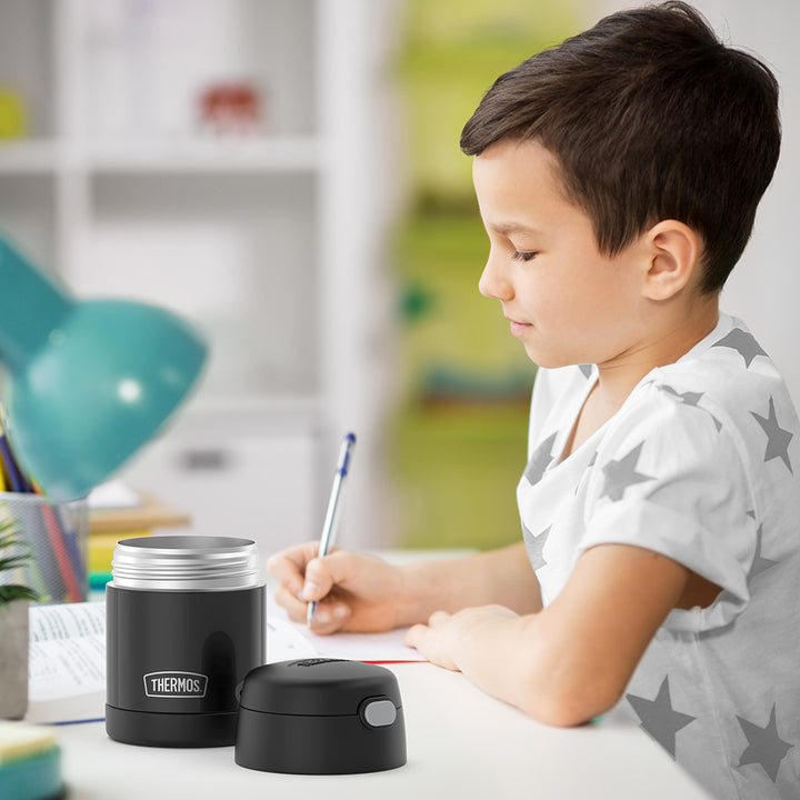 10 ounce Funtainer food jar open on a table next to a boy doing homework.