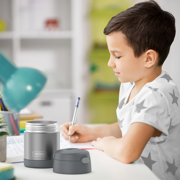 10 ounce Funtainer food jar open on a table next to a boy doing homework.