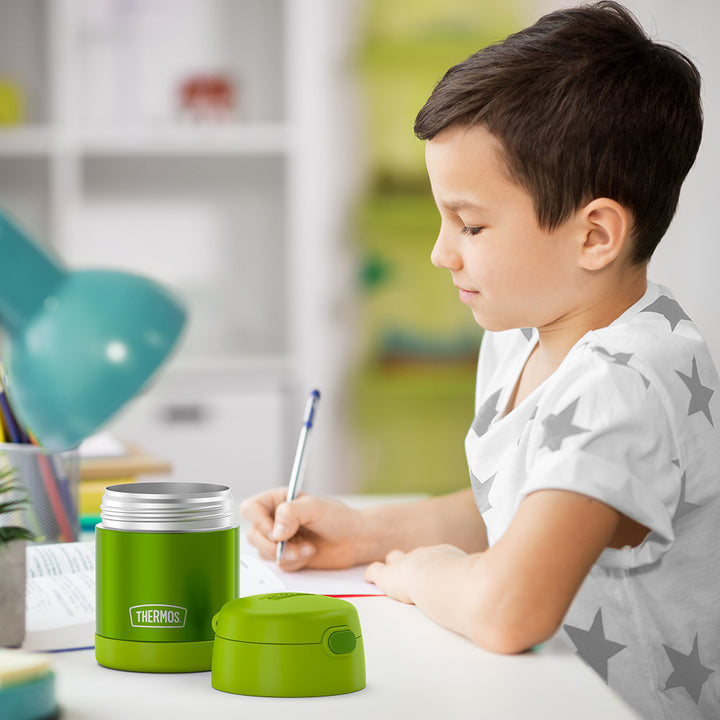 10 ounce Funtainer food jar open on a table next to a boy doing homework.