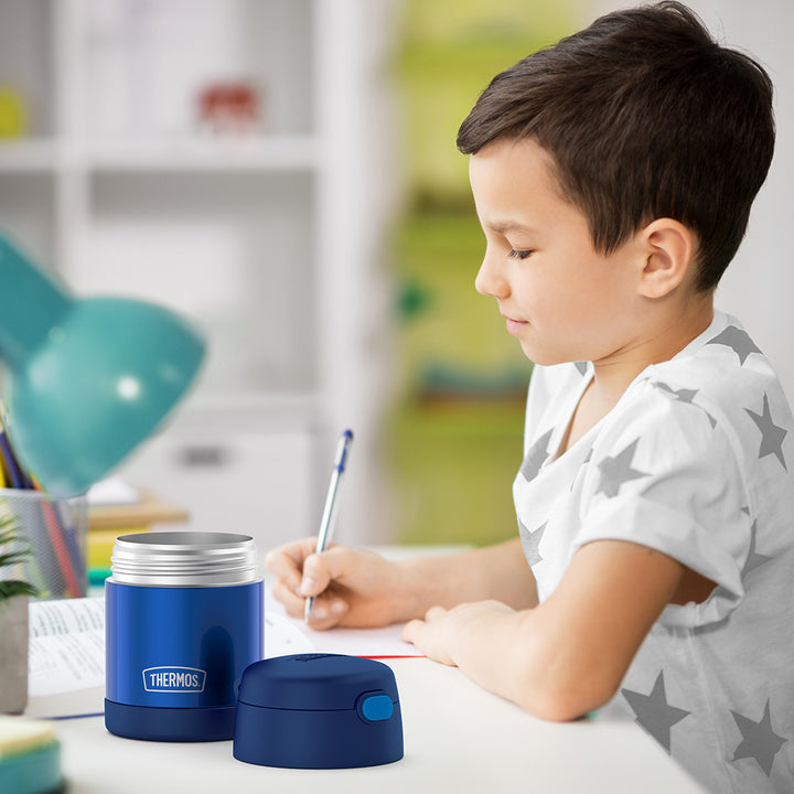 10 ounce Funtainer food jar open on a table next to a boy doing homework.