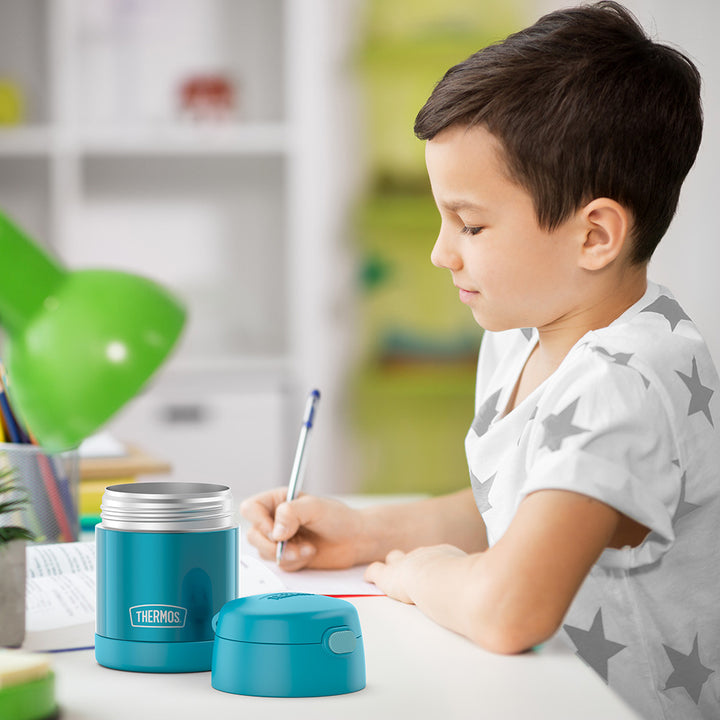 10 ounce Funtainer food jar open on a table next to a boy doing homework.