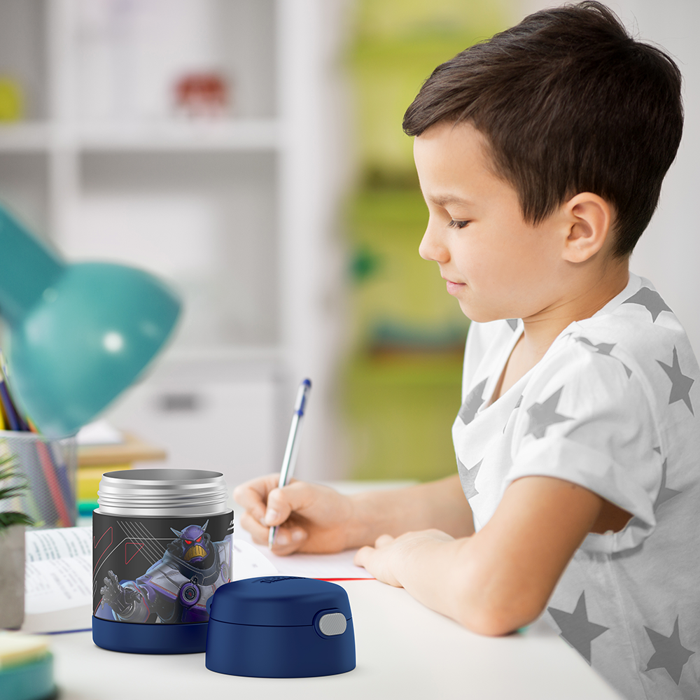 Boy sitting at table doing homework with an open 10 ounce Funtainer food jar open next to him.
