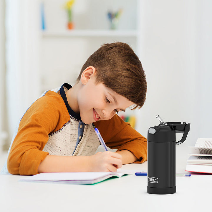 Boy sitting at a table doing homework, with a black 12 ounce Funtainer water bottle opened next to him.