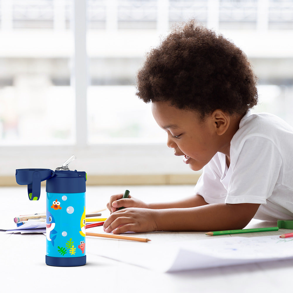 Boy sitting at a table coloring, with the 12 ounce Funtainer Baby Shark water bottle opened next to him.