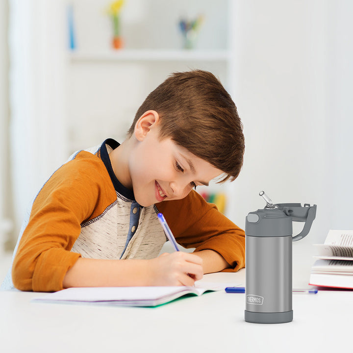 Boy sitting at a table doing homework, with a grey 12 ounce Funtainer water bottle opened next to him.