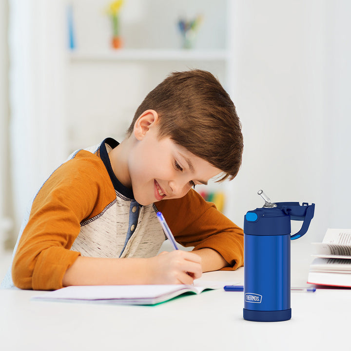 Boy sitting at a table doing homework, with a blue 12 ounce Funtainer water bottle opened next to him.