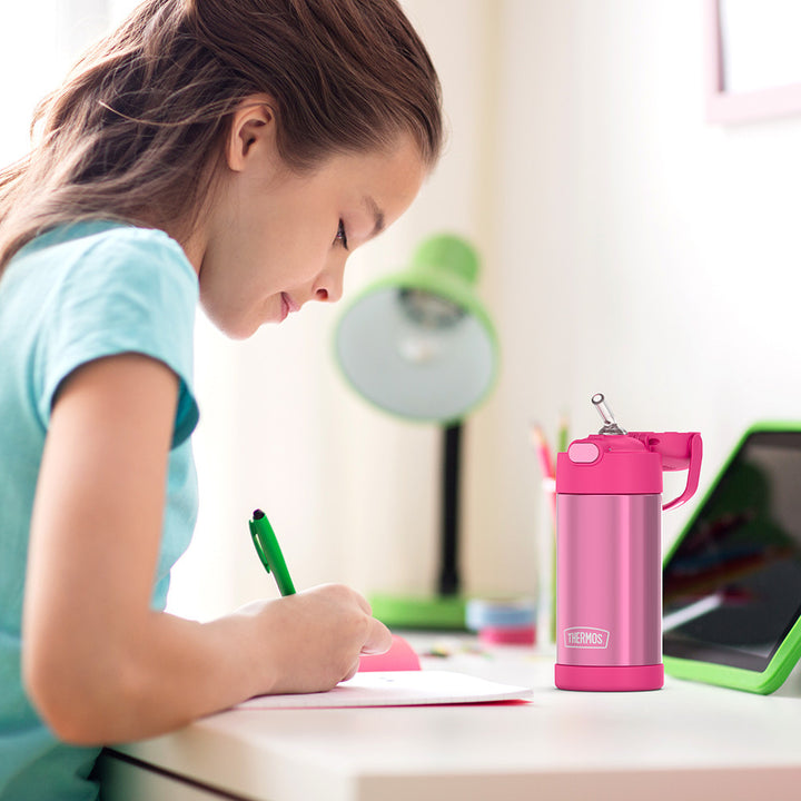 Girl sitting at a table doing homework, with a 12 ounce pink Funtainer water bottle opened next to her.