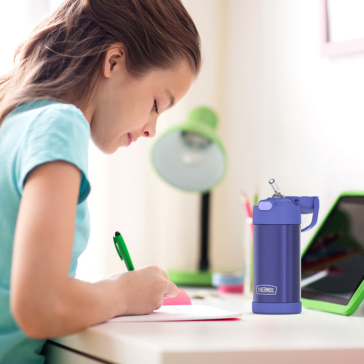 Girl sitting at a table doing homework, with a 12 ounce purple Funtainer water bottle opened next to her.