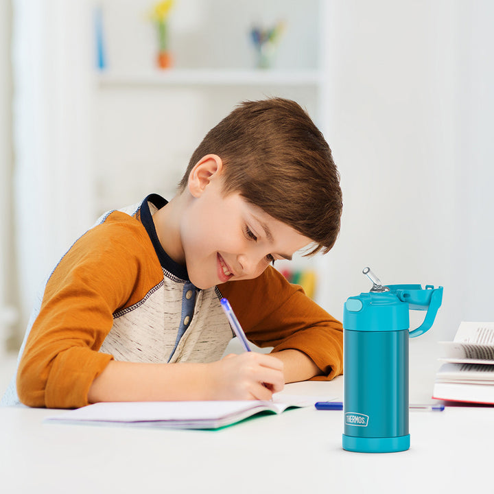 Boy sitting at a table doing homework, with a teal 12 ounce Funtainer water bottle opened next to him.
