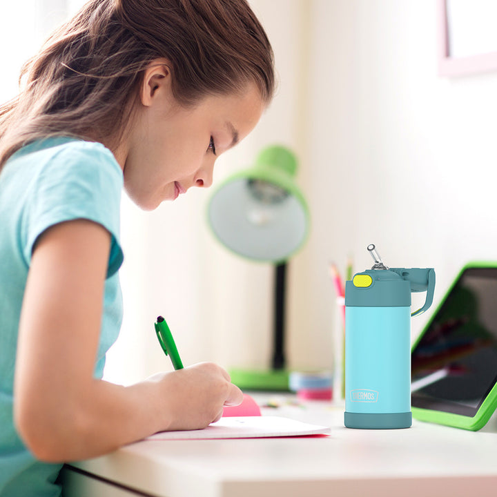 Girl sitting at a table doing homework, with a 12 ounce blue and green Funtainer water bottle opened next to her.