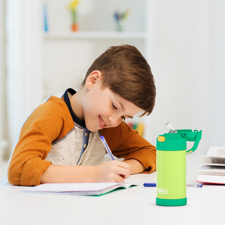 Boy sitting at a table doing homework, with a lime and orange 12 ounce Funtainer water bottle opened next to him.