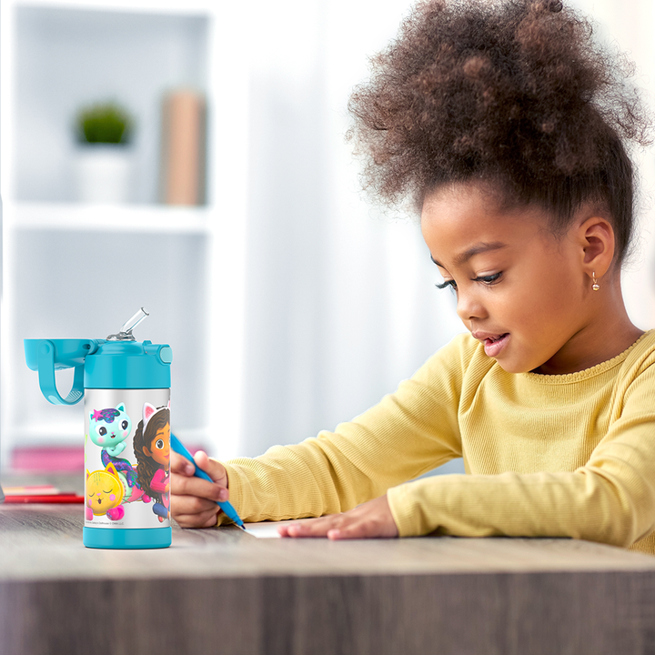 Girl sitting at a table doing homework, with a 12 ounce Gabby's Dollhouse - Blue Funtainer water bottle opened next to her.