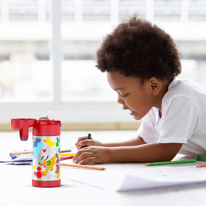 Boy sitting at a table coloring, with the 12 ounce Funtainer Preschool Mickey Mouse, Red water bottle opened next to him.